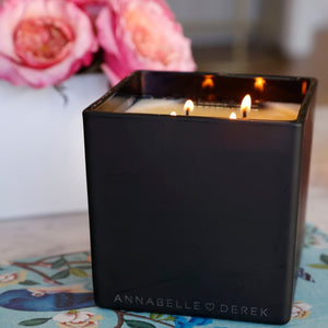 pictured option 2, annabelle heart derek on the bottom of this beautiful black candle. the candle is lit on its 4 wicks with flowers in the background