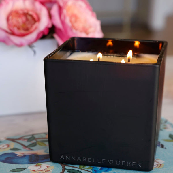 pictured option 2, annabelle heart derek on the bottom of this beautiful black candle. the candle is lit on its 4 wicks with flowers in the background