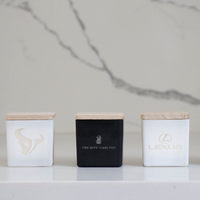 Three TAJA mini logo candles on marble: Houston Texans, The Ritz-Carlton and Lexus