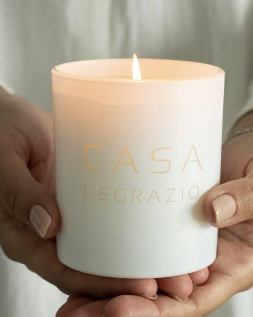 Two hands holding a lit white Casa candle