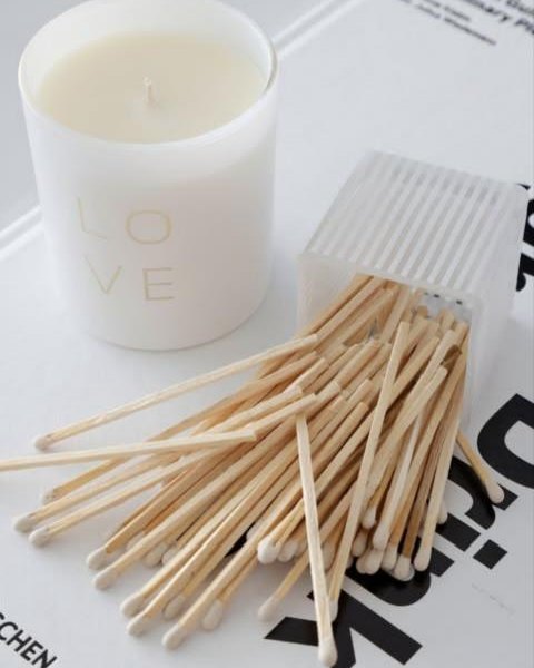 A white LOVE candle with matches spilling from a ribbed holder