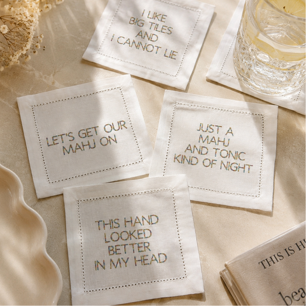 Four white embroidered square coasters with humorous text about mahjong.