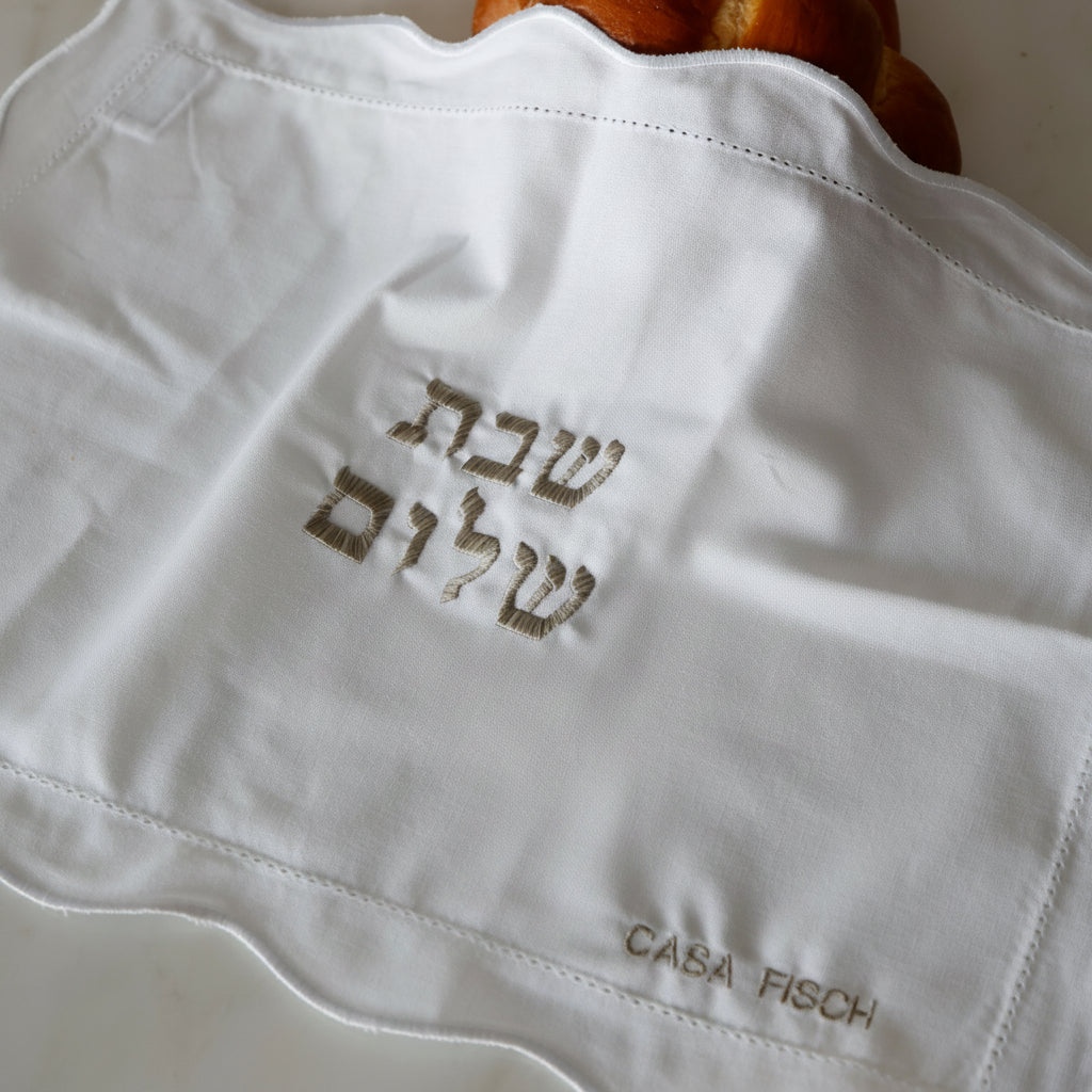 White linen challah cover with embroidered text.