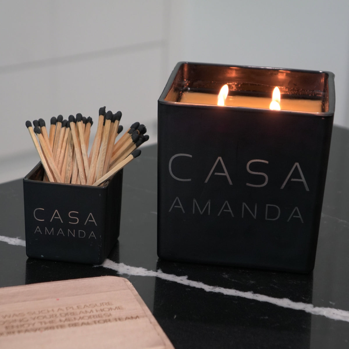 Lit black Casa candle engraved Amanda beside its match holder