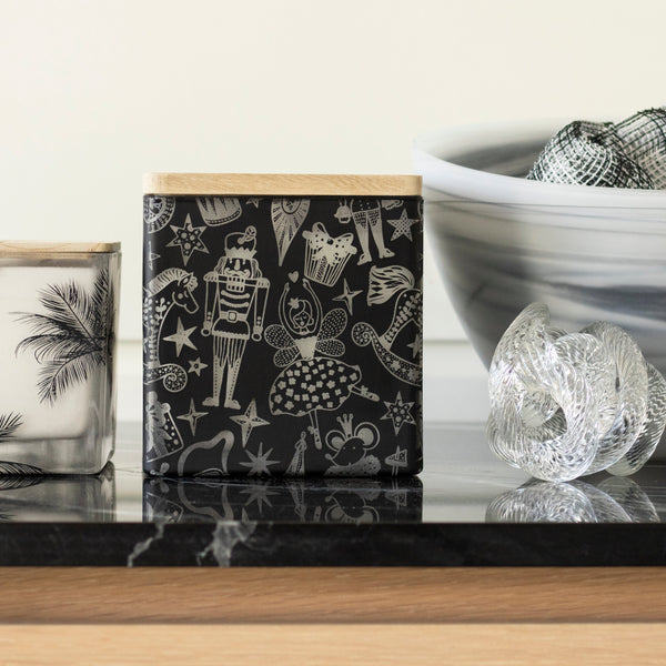 Two decorative glass boxes with black and white patterns, one featuring palm trees and the other nutcracker illustrations, styled on a black marble surface next to a bowl of mesh fabric.