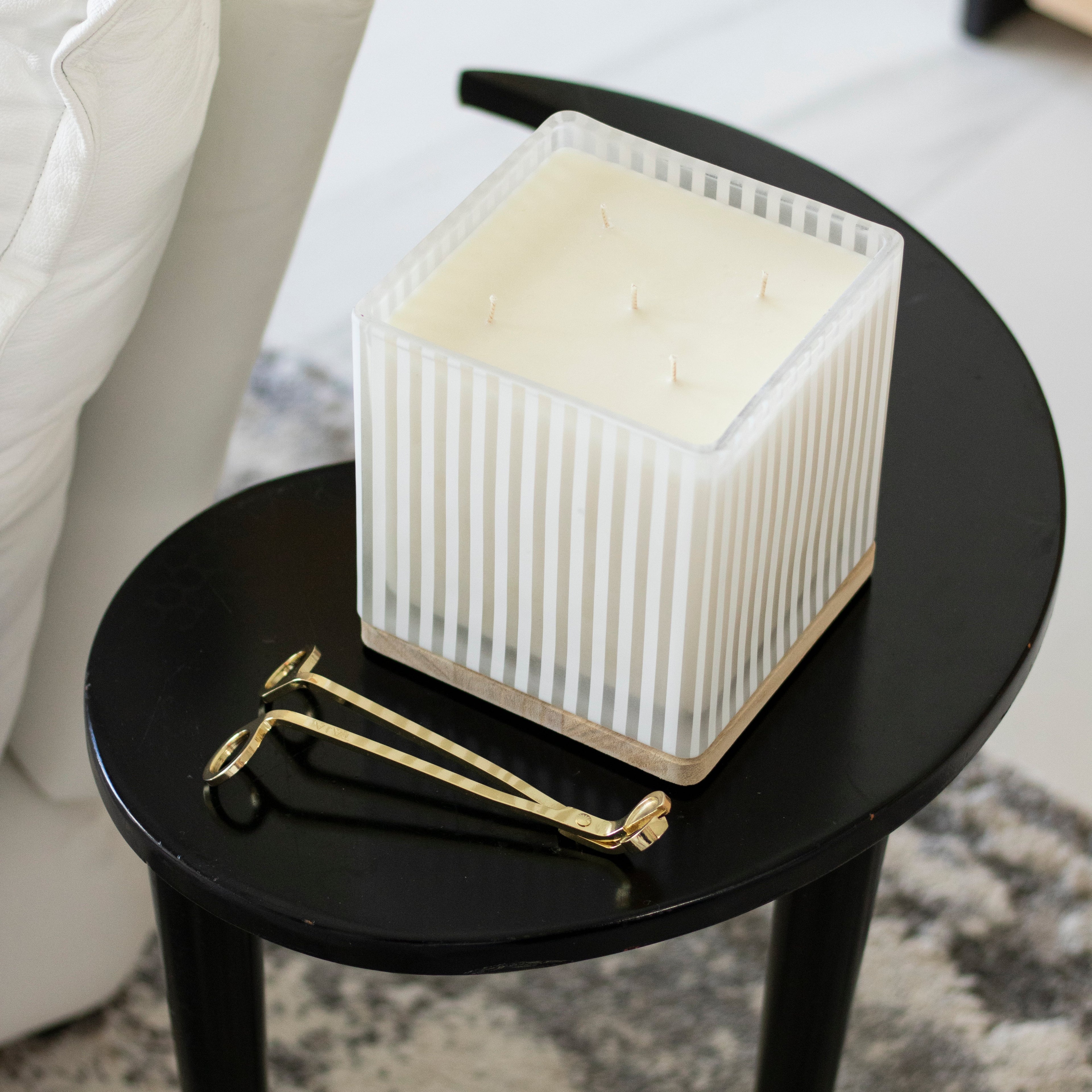 Square candle with stripes on a black side table in a home setting with gold wick trimmer