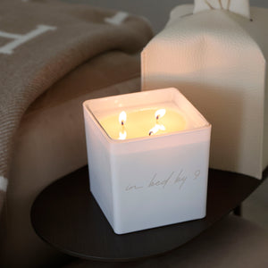 "in bed by 9" engraved on the front of white grande size candle in TAJA's ballet font