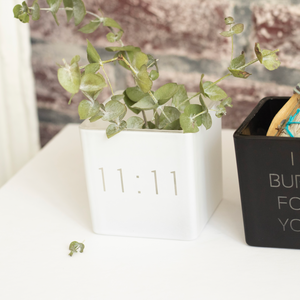 white vase with 11:11 engraved on the front, filled with eucalyptus plants. next to it black smudge kit i burn for you
