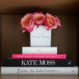 I'm a cool mom white super vase reused as a flower vase. beautifuly decorated on a shelf with Rizzoli books