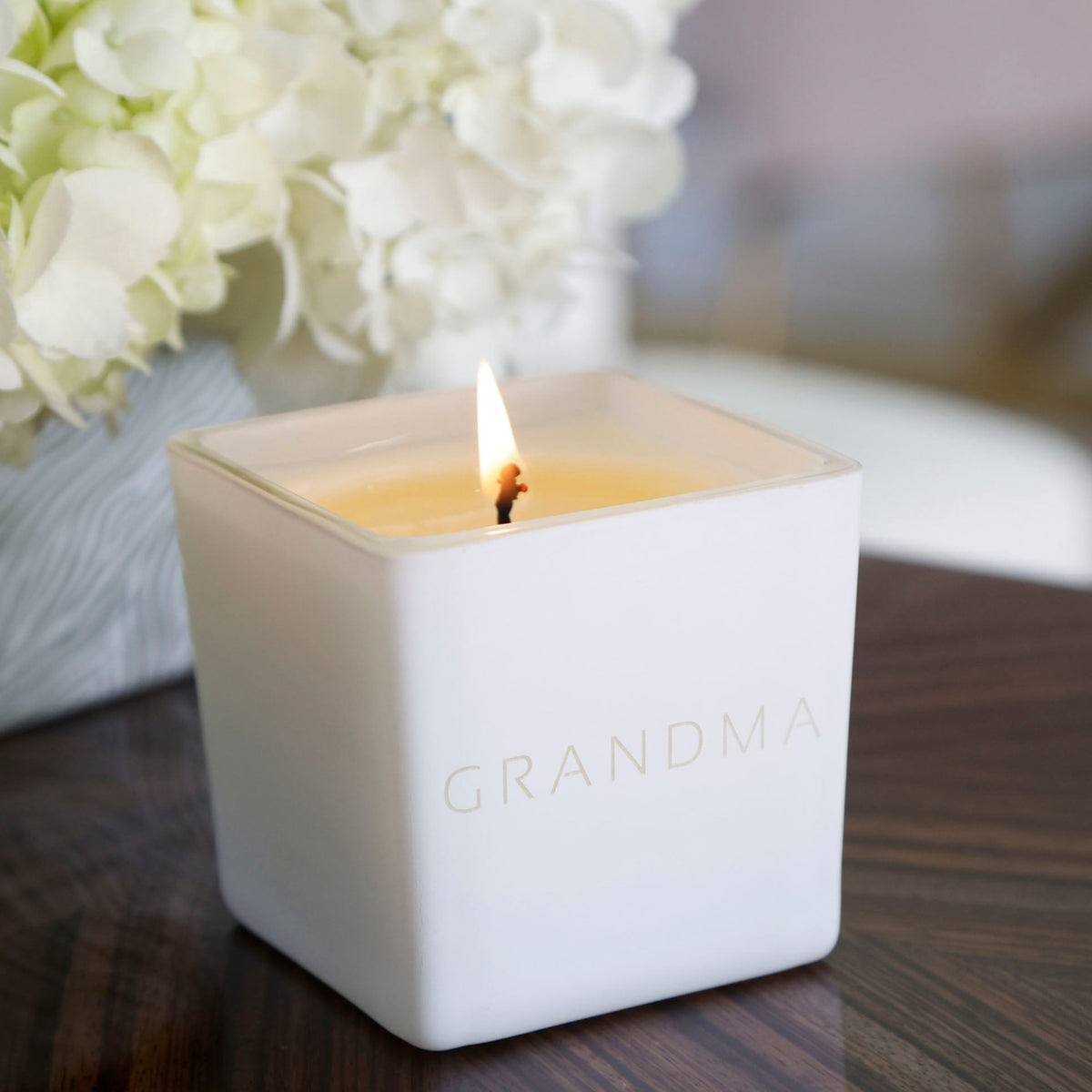 Lit white candle engraved Grandma beside white hydrangeas