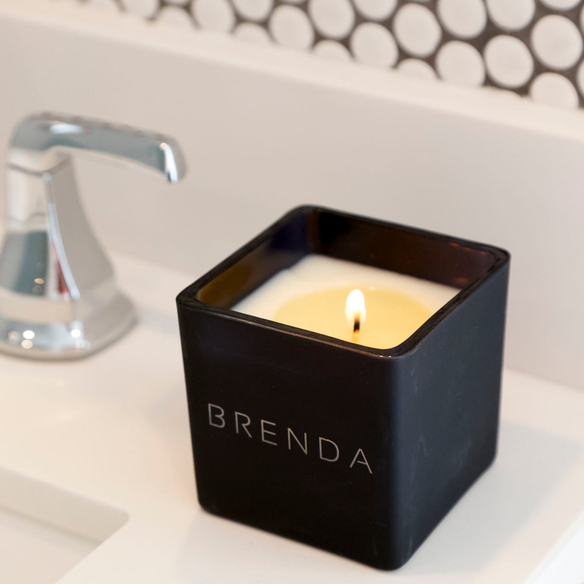 Lit black candle engraved Brenda on a bathroom counter