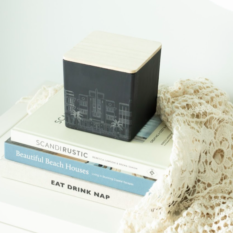 black miami skyline candle on top of 3 stacked books next to a beach bag