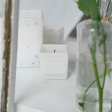 white grateful repeat candle next to a vase with a plant and next to white candle 