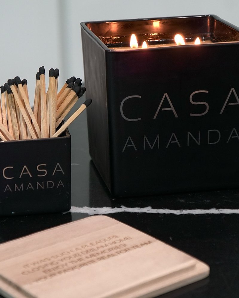 A lit black Casa candle engraved Casa Amanda, with its match holder and a wooden coaster