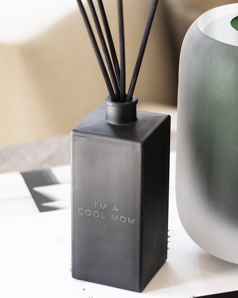 A black diffuser engraved I'm a Cool Mom beside a green glass vase