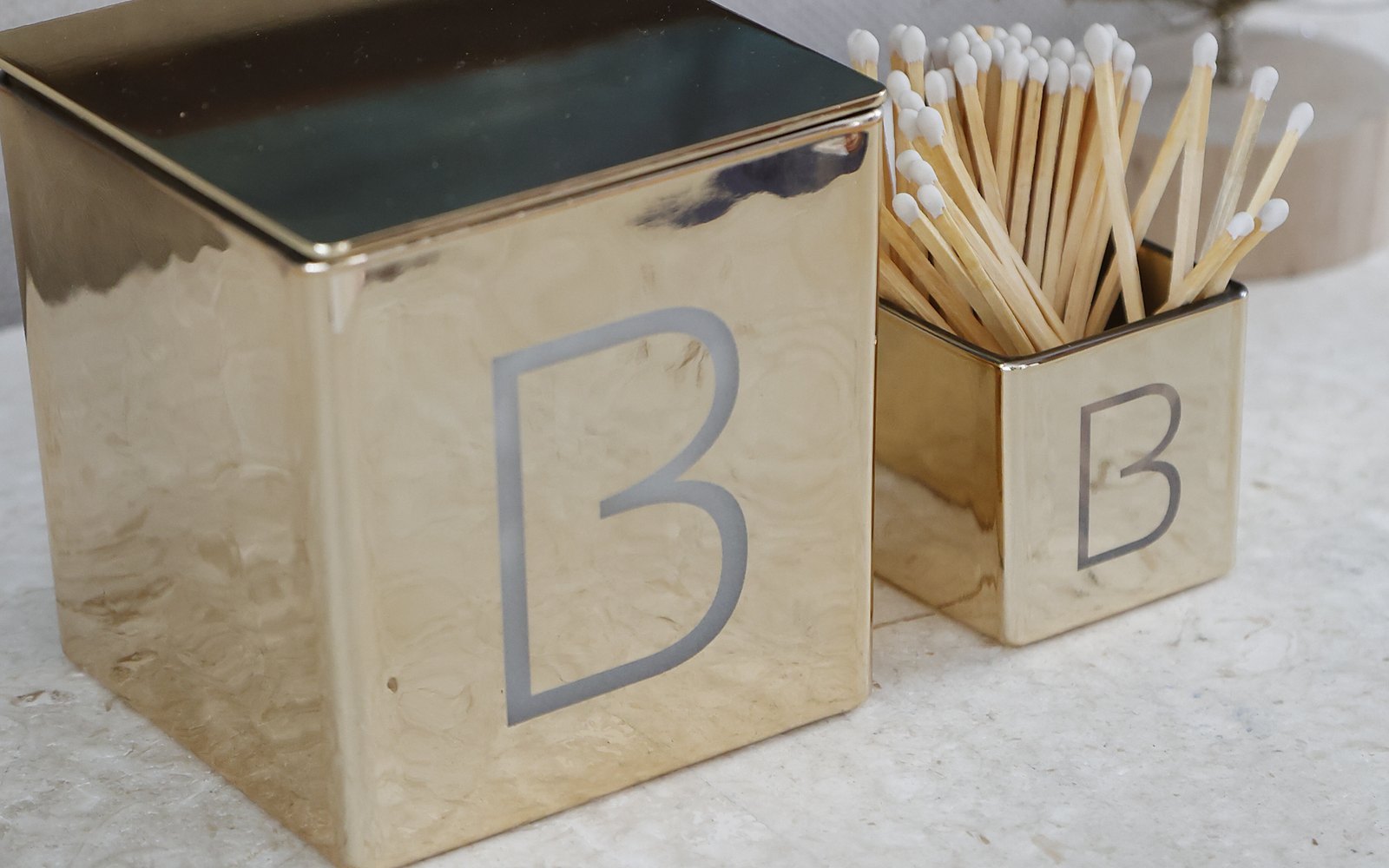 A gold candle and match holder, each engraved with the letter B