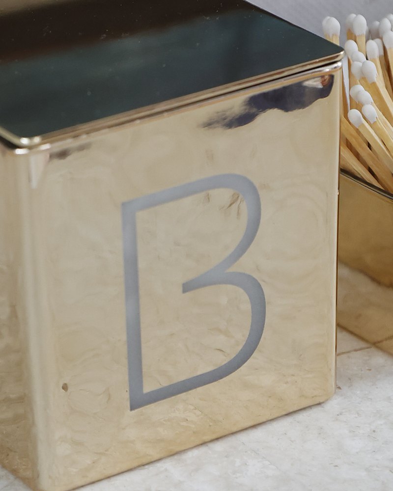 A gold candle and match holder, each engraved with the letter B