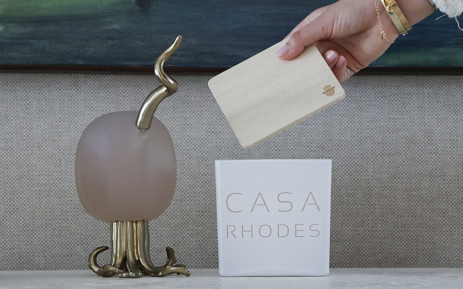 A hand setting the wooden lid on a white candle engraved Casa Rhodes