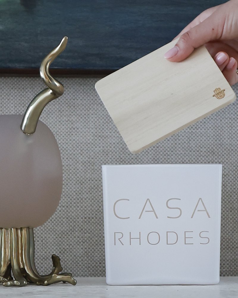 A hand setting the wooden lid on a white candle engraved Casa Rhodes